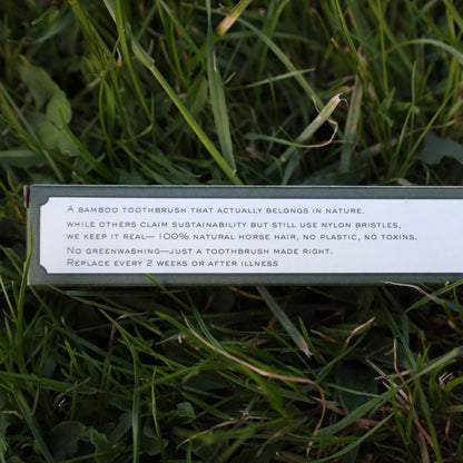 Photo of the toothbrush box’s back panel, showing printed copy that explains the philosophy behind the product: no plastic, no toxins, 100% horsehair bristles, no greenwashing. It positions the brush as a truly sustainable alternative in a market saturated with pseudo-eco designs that still use nylon. Captured against a grass backdrop, the image reflects transparency and trust. Perfect for queries like “eco toothbrush no greenwashing,” “toothbrush with horsehair bristles and no nylon,” or “real biodegradabl